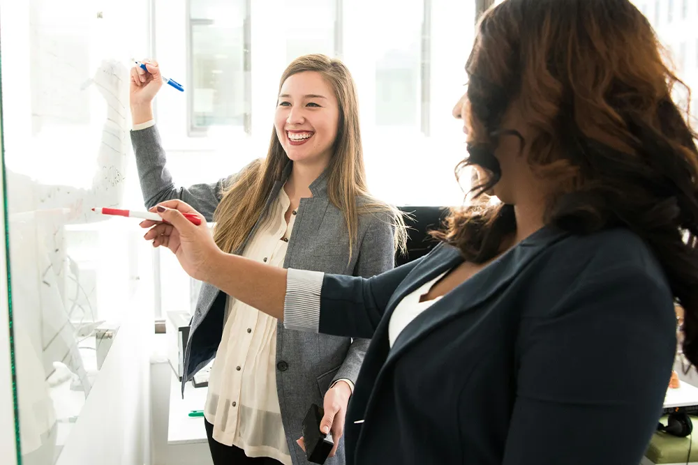 Marketing consultant standing at whiteboard laughing with client as they map out workflows